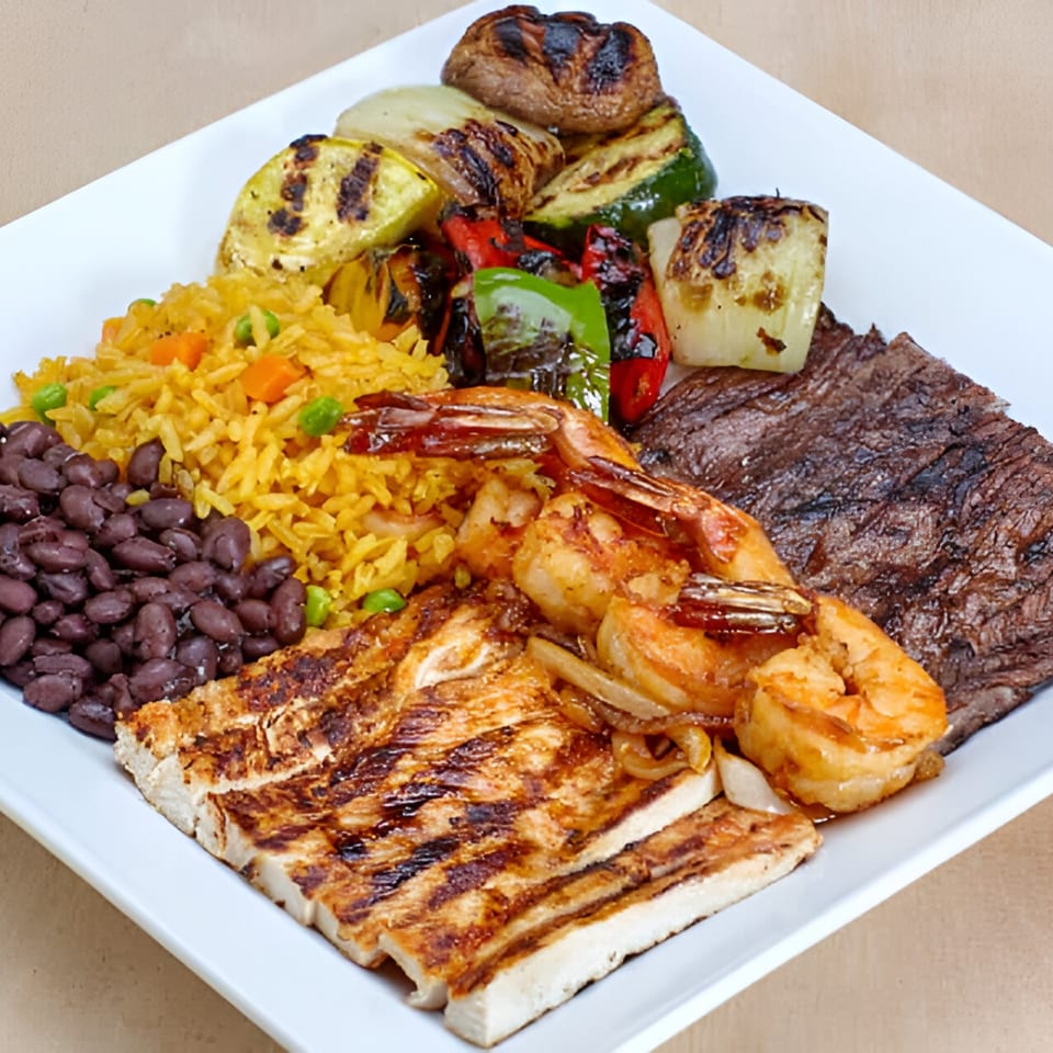 A Las Fajitas combo plate with grilled chicken, steak, shrimp, rice, black beans, and vegetables.