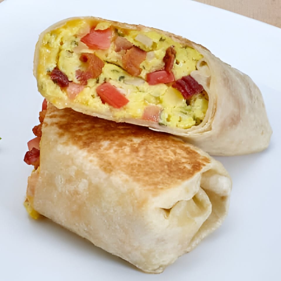 A breakfast burrito from Las Fajitas, cut in half, revealing scrambled eggs, bacon, and tomatoes.
